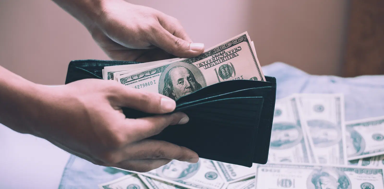 An assortment of various US dollar denominations fans out from an open brown leather wallet on a dark surface
