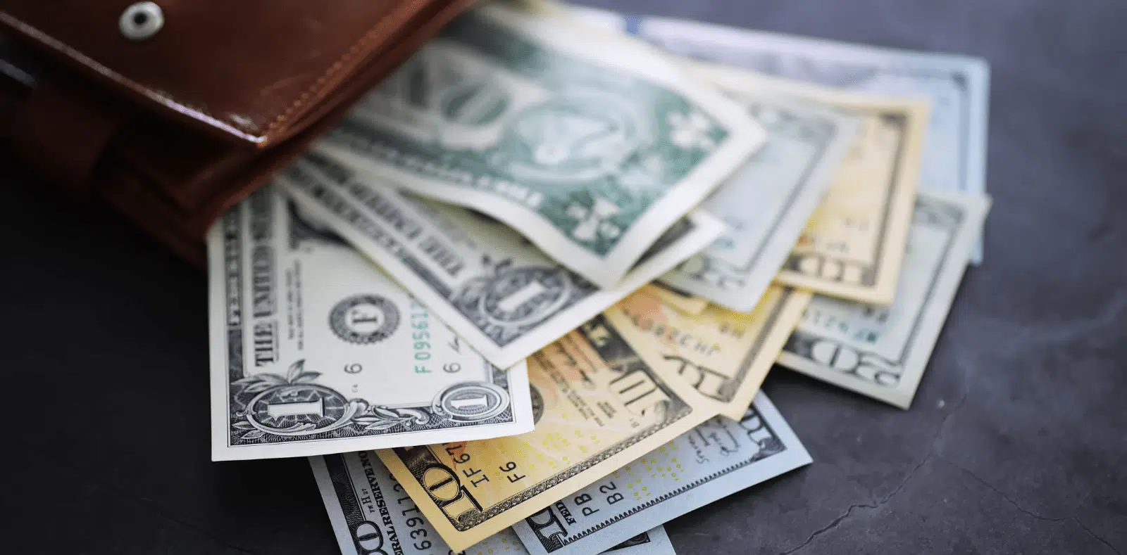 A smiling blonde woman leans over a man's shoulder as he reads a document and holds a pen near a laptop with coffee mugs nearby