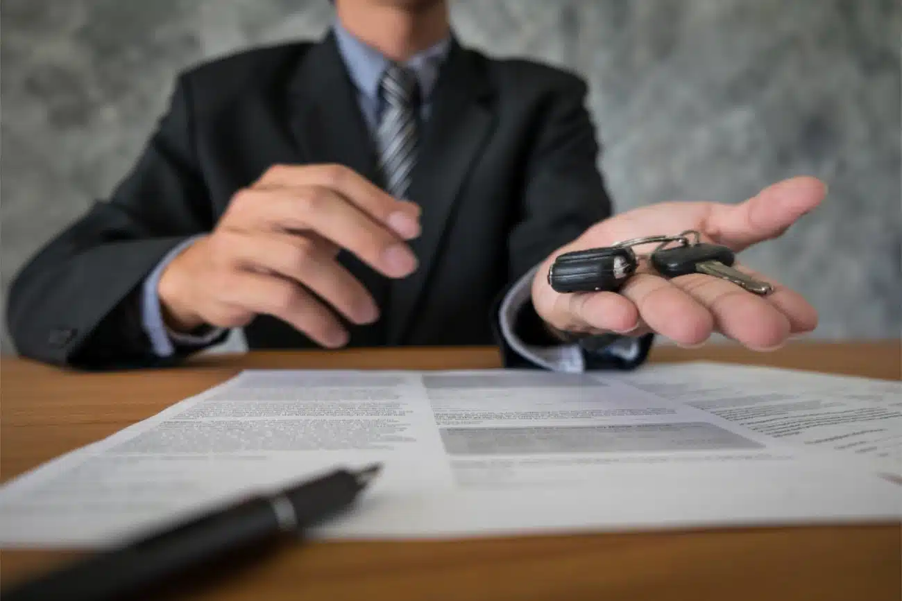 Car keys and a loan agreement document on a wood desk, with a pen and calculator visible, horizontal format, warm lighting