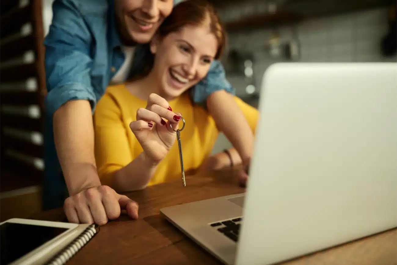 Person using a laptop to fill out a loan application, car keys on desk beside them, bright natural light, horizontal format