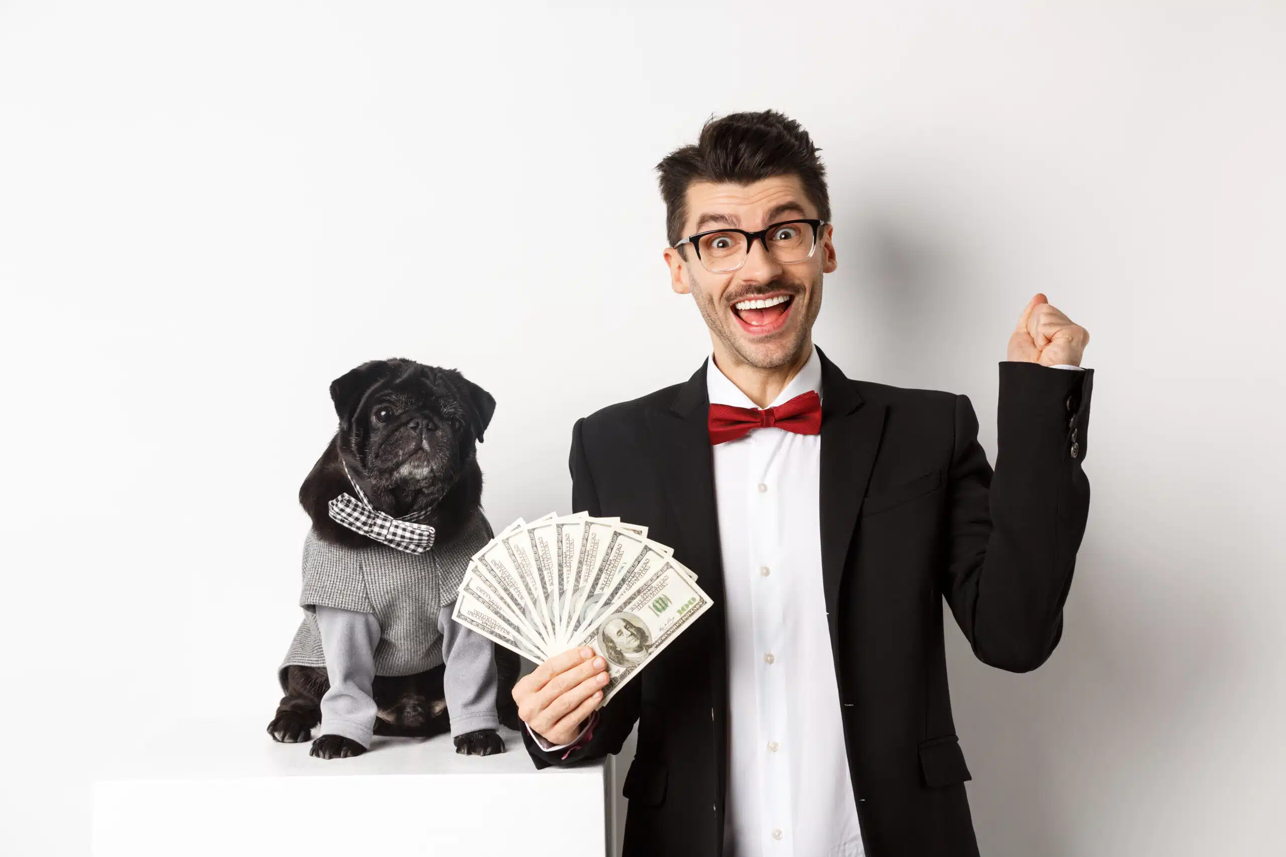 Man in a suit holding bills while posing next to a dog against a white background.