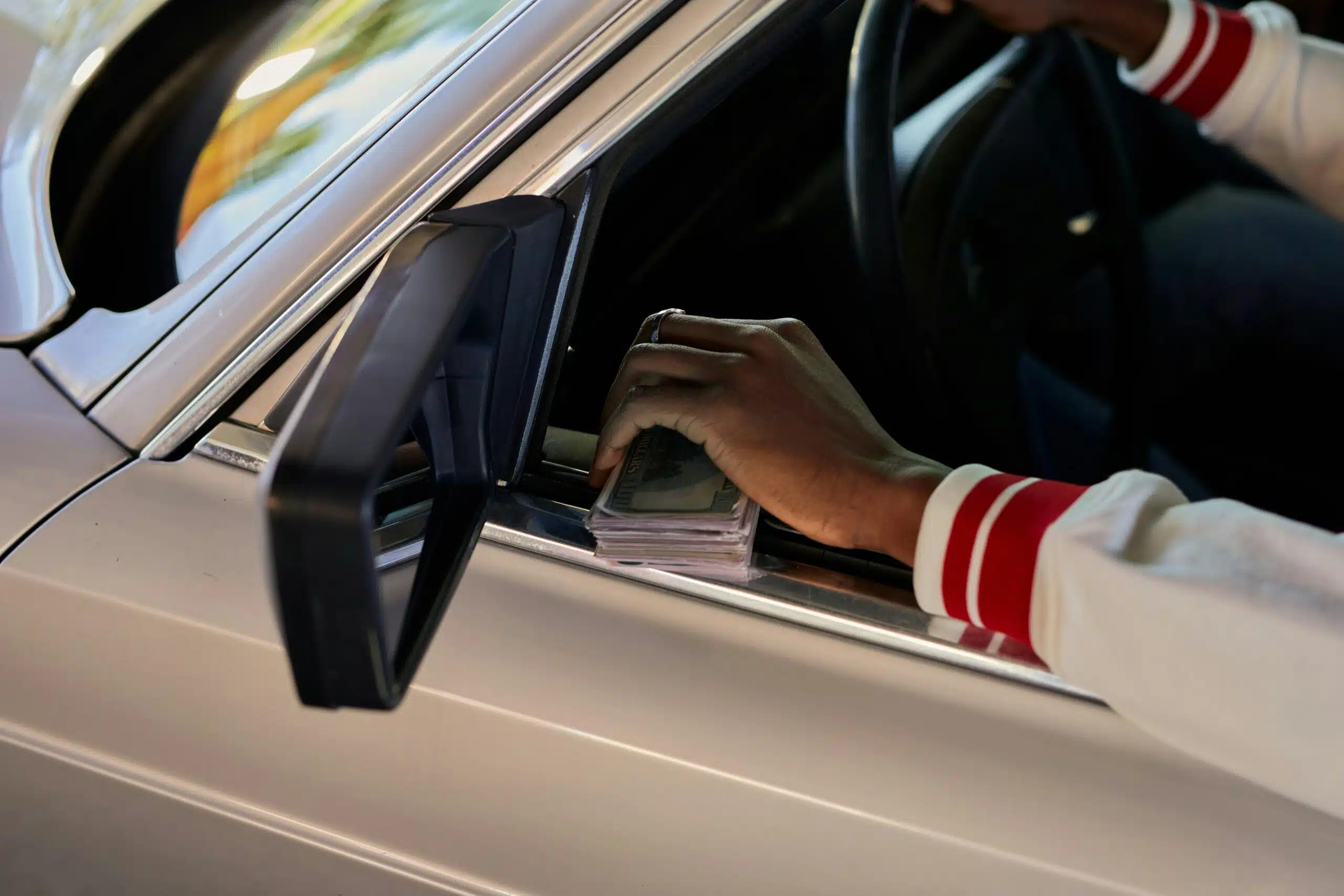 Hand holding a stack of bills through a car window