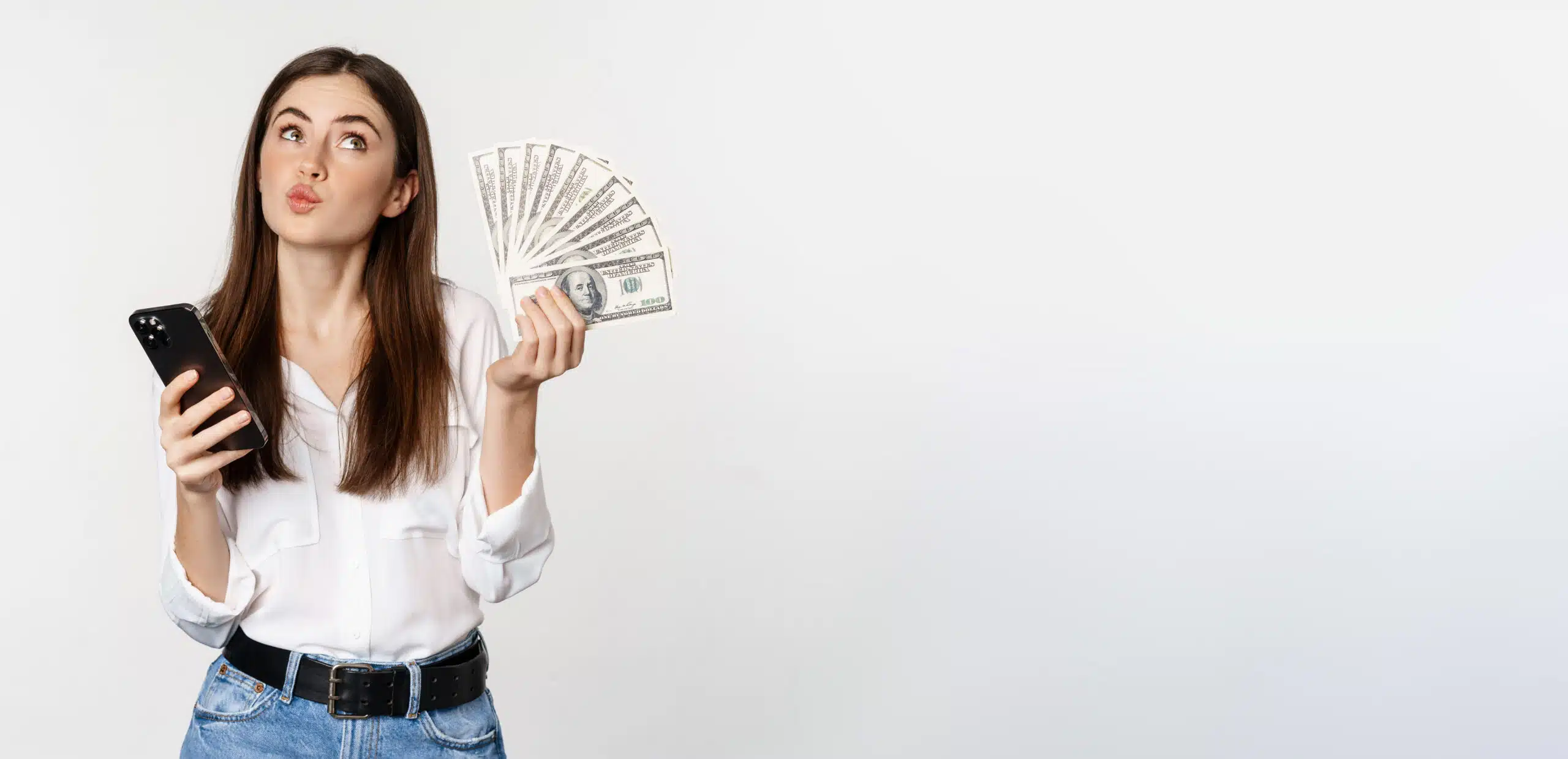 Woman looking to the side while holding a mobile phone and several bills against a light gray background.